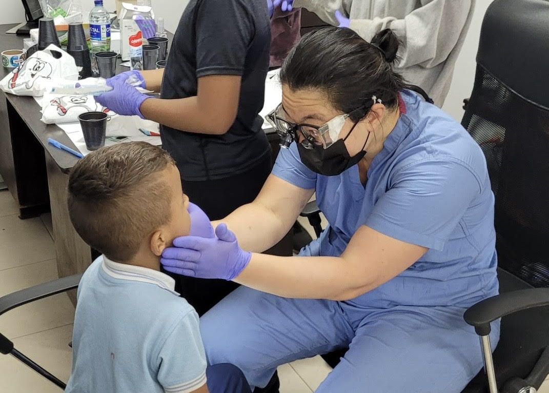 A woman in scrubs providing dental care to a child while wearing a medical mask.